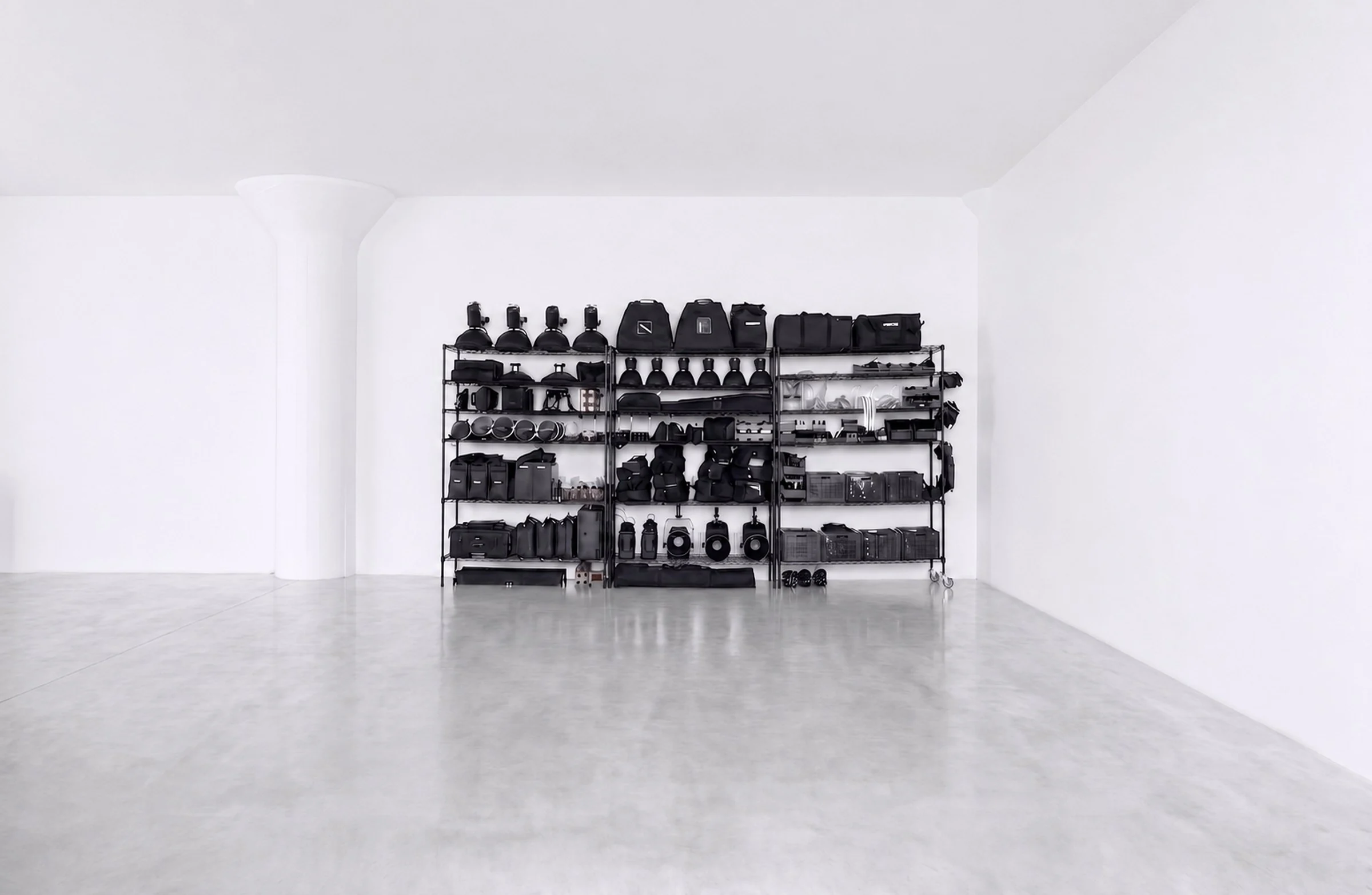 Lighting and grip gear on wire shelves against the white wall of the shooting floor