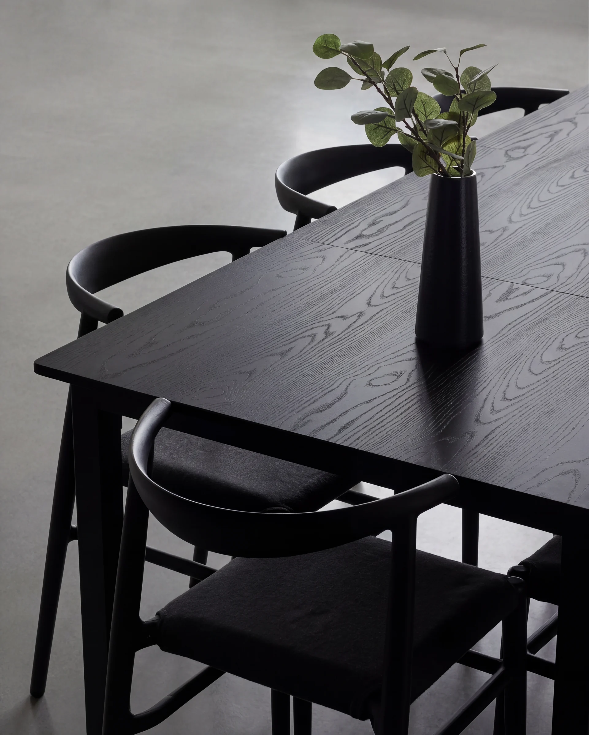 A black dining table and chairs with olive branches in a vase