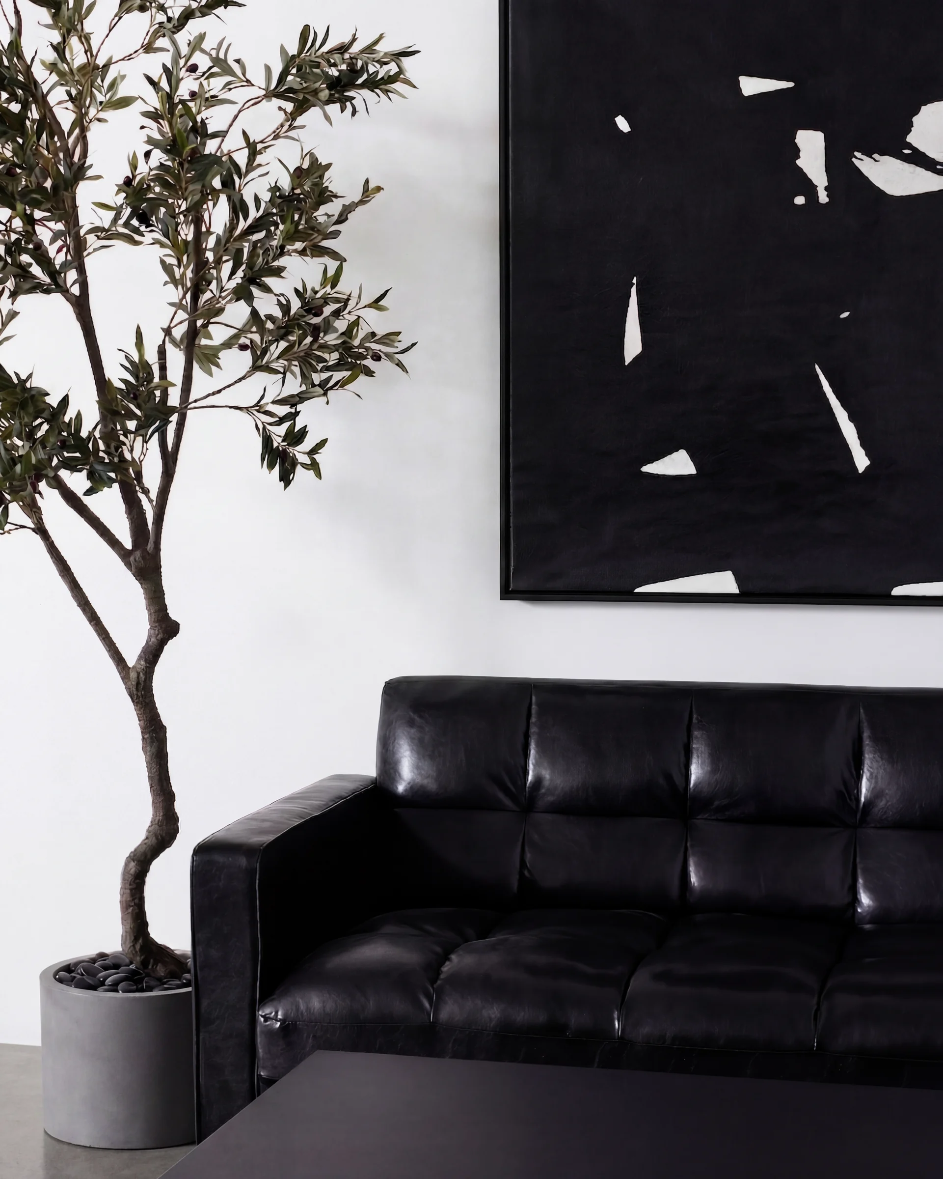 A black leather sofa and an olive tree under a large black-and-white painting